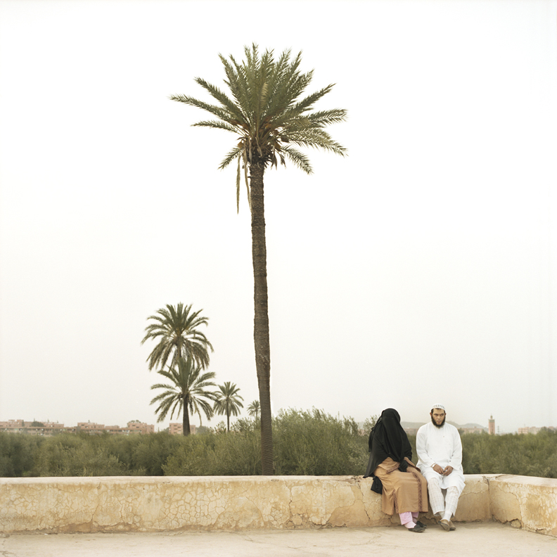 Couple assis sur un mur devant des palmiers verts ciel blanc